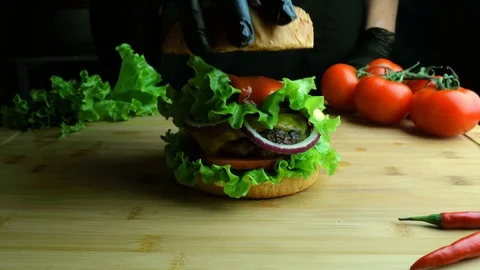 Chef in black gloves and apron is preparing a burger on a cutting board. Vídeo Stock 112002725