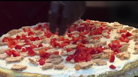 Chef in black gloves in cafe kitchen puts fresh red strawberry pieces on cake Stock Footage 308923353