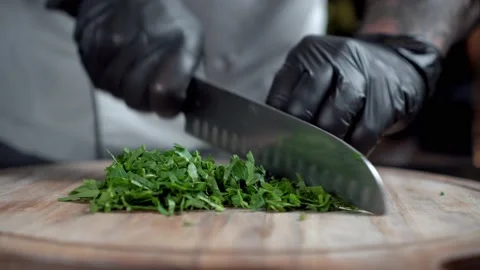 A chef in black gloves chops parsley on wooden cut board Stock Footage 168840063