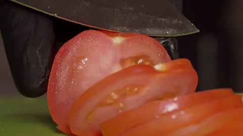 Chef in black gloves cuts a ripe tomato with a large knife, close up Stock Footage 142732929