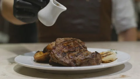 A chef in black gloves pours steak sauce on a plate with grilled vegetables Stock Footage 118791975