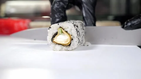 A chef in black gloves prepares sushi, he slices sushi with a large knife. Stock Footage 321814746