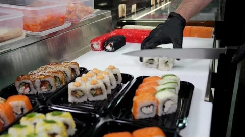 A chef in black gloves prepares sushi, he slices sushi with a large knife. Stock Footage 321815236