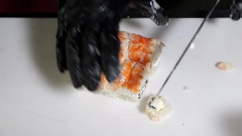 A chef in black gloves prepares sushi, he slices sushi with a large knife. Stock Footage 325181475