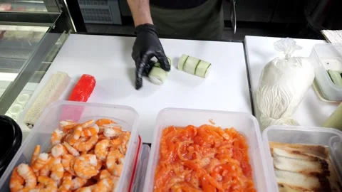A chef in black gloves prepares sushi, he slices sushi with a large knife. Stock Footage 326414556