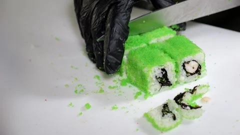 A chef in black gloves prepares sushi, he slices sushi with a large knife. Stock Footage 329276575