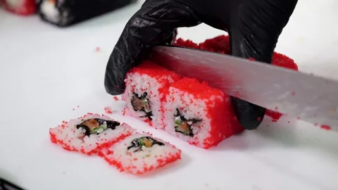 A chef in black gloves prepares sushi, he slices sushi with a large knife. Stock Footage 346443062