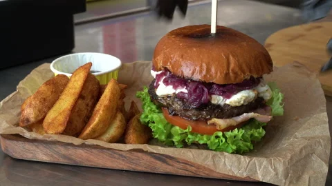 The chef in black gloves puts a burger on a board with rustic potatoes and sauce Video stock 178535778