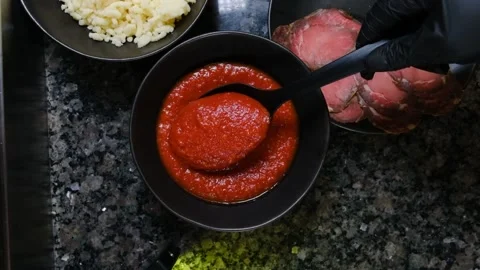 Chef in black gloves puts red sauce with a spoon from a pizza plate slow motion Stock Footage 230076212