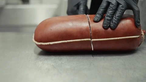 Chef in black gloves slices through a cylindrical meat product revealing Vídeo Stock 332724230
