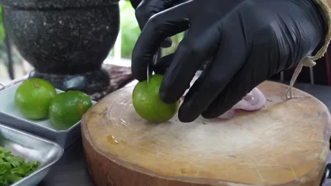Chef in black gloves slicing fresh lime on a rustic wooden cutting board during Stock Footage 338211873