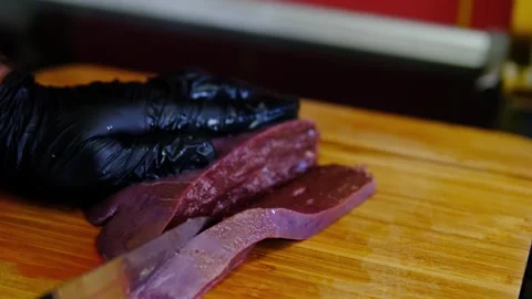 Chef in black gloves slicing fresh raw beef liver on wooden cutting board Stock Footage 346265139