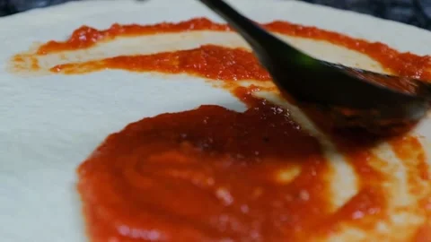 Chef in black gloves spreads red sauce with a spoon over pizza dough slow motion Stock Footage 230076247
