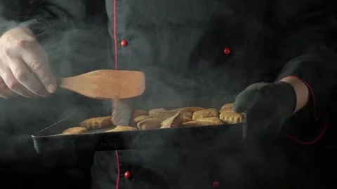 Chef in black uniform lifts tray of freshly baked cookies, using wooden spatula Stock Footage 334070192