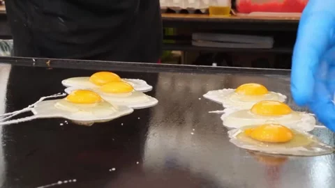Chef in Blue Gloves Cracking Fresh Eggs on Flat Top Griddle Video stock 347688925