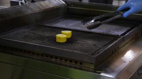 A chef in blue gloves roasts pieces of corn cobs and turns them over on the gril Stock Footage 130903755