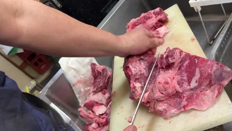 Chef breaking down a large block of raw beef with a knife on a cutting board Stock-Footage 337399853