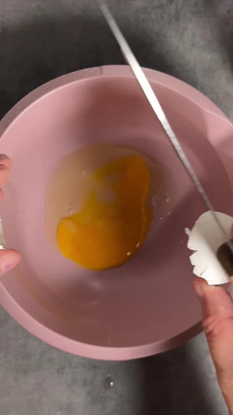 Chef breaks white egg with knife on table and yolk falls into pink bowl Stock Footage 328534460