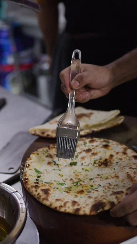 Chef Brushing Melted Butter onto Freshly Baked Garlic Naan Bread Stock Footage 345699780