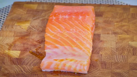 A chef brushing a salmon steak with olive oil on a wooden cutting board. Stock Footage 315903839