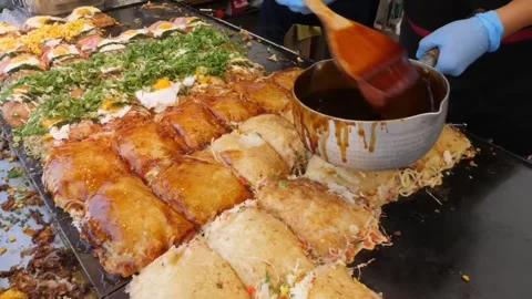 Chef Brushing Savory Glaze on Hiroshima-Style Okonomiyaki at a Busy Japanese Str Stock Footage 347688904