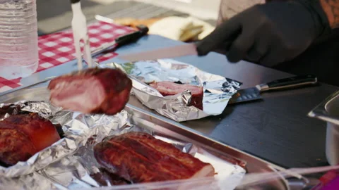 Chef carving juicy cooked pork belly on a metal table, preparing it for sale at Vidéo 339783653