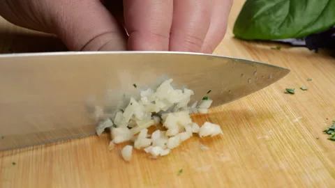 Chef chopping fresh garlic cloves on a wooden cutting board.  库存影片 341479769