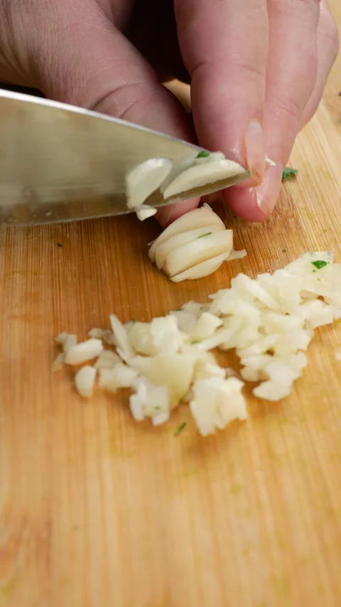 Chef chopping fresh garlic cloves on a wooden cutting board. Stock Footage 341480333