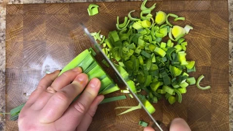 Chef chops leek stems with a cleaver on wooden cutting board. Stockbeeldmateriaal 302273678