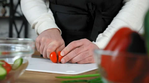 Chef cook man in black apron sliced fresh cherry tomato on board in home kitchen Stock Footage 149662197