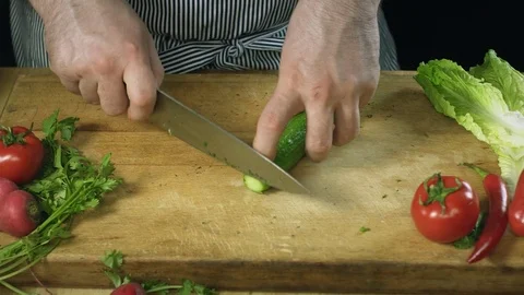 Chef cook professionally slicing a cucumber with a chef's knife on cutting board Stock Footage 76963697