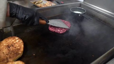 Chef cooking and smashing a raw beef burger patty on a hot griddle in a kitchen Stock Footage 337900231