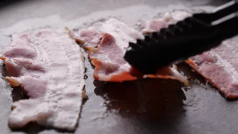 Chef cooking bacon strips for breakfast. Sizzling and smoking in a hot pan Stock Footage 128406404