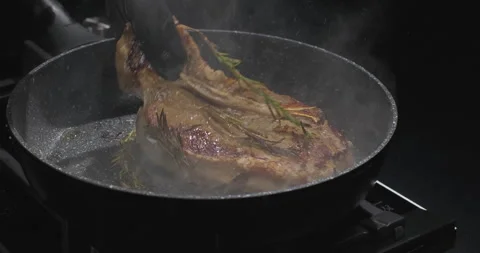 Chef cooking beef t-bone steak with rosemary on a pan over black background Stock Footage 250002034