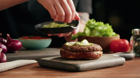 Chef cooking burger, putting sliced cucumber on meat, making sandwich, fast food Stock Footage 170329092