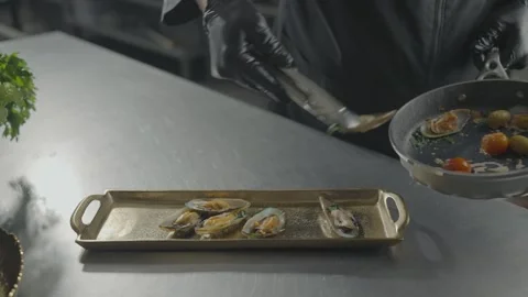 Chef in cooking gloves puts cooked mussels with tongs on serving dish. Slow Stock Footage 241723534