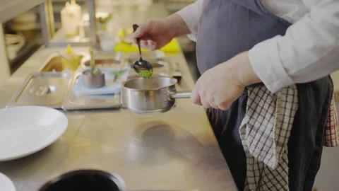 A chef is cooking in a kitchen with a silver pot on the counter Stock Footage 306576986