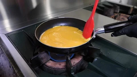 Chef cooking scrambled eggs in a frying pan on gas stove in commercial kitchen Stock Footage 324711059