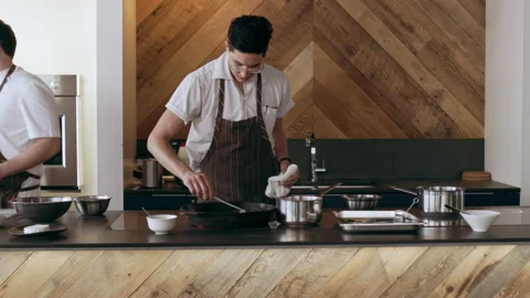 Chef cooking sliced shallots in a hot pan in interior kitchen with soft day ligh Stock Footage 199459476