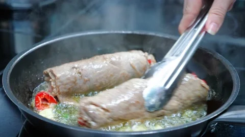 Chef is cooking two meat rolls in oil on a frying pan, close-up in slow motion Stock Footage 150953097