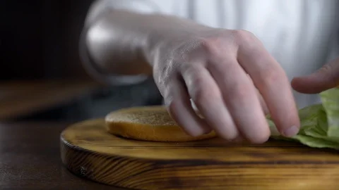 Chef cooks burger and puts leafs of fresh green salad to the bun, making burgers Stock Footage 106802736