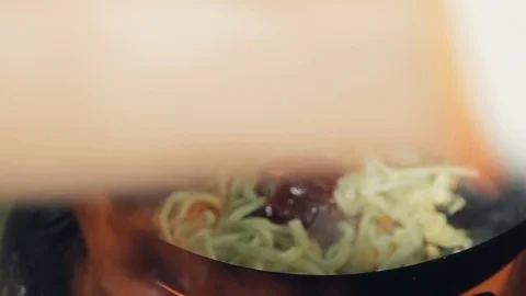 Chef cooks in fired up wok the noodles and Adds sauce and mixes it. Selective Stock Footage 128985133