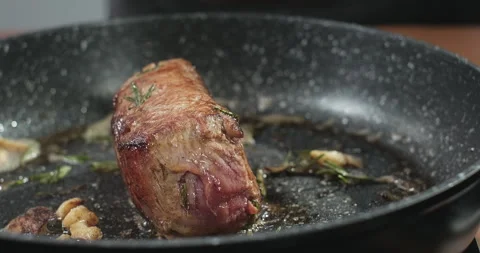 Chef cooks juicy beef steak with rosemary and garlic on a frying pan. Slow Stock Footage 254544647
