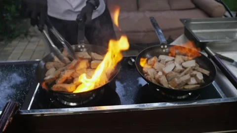 Chef cooks meat on an open fire in a burning pan outdoors in slow motion Video stock 142186126