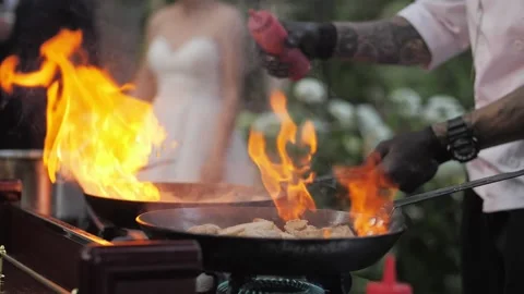 Chef cooks meat on an open fire in a burning pan outdoors in slow motion Video stock 142186157