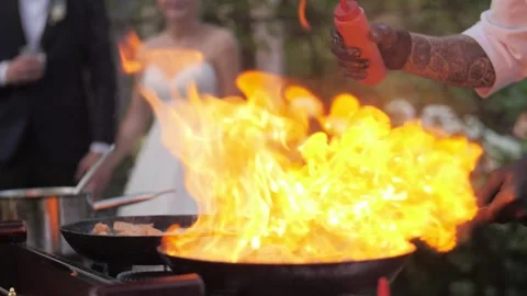 Chef cooks meat on an open fire in a burning pan outdoors in slow motion Video stock 142799273