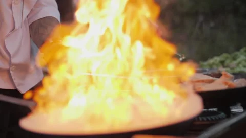 Chef cooks meat on an open fire in a burning pan outdoors in slow motion Stock Footage 142799422