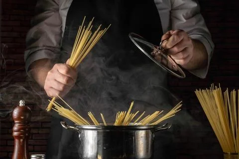 Chef cooks pasta in a pot while steam rises in an indoor kitchen setting du.. Stock Photos