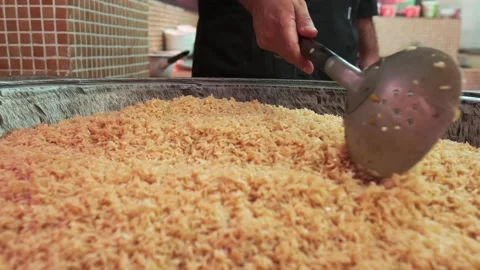 The chef cooks pilaf in a large cauldron with a slotted spoon Stock Footage 253369161