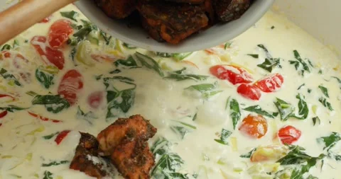 Chef cooks tomatoes, spinach, and salmon in creamy sauce, stirring with a wooden Stock Footage 319388575
